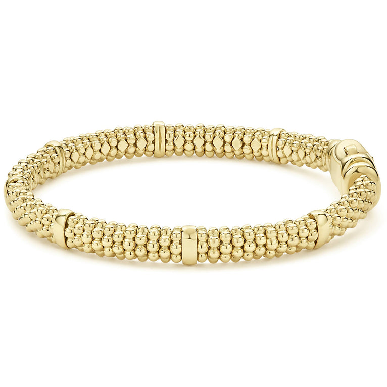 An 18k gold bracelet resting in the middle of a white background. The bracelet features smooth stations and caviar beading.