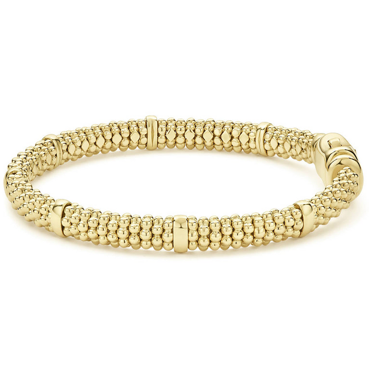 An 18k gold bracelet resting in the middle of a white background. The bracelet features smooth stations and caviar beading.