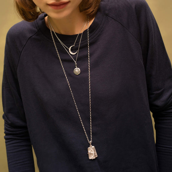 A woman wearing a silver Locket necklace accented with White sapphire, a compass motif, and a sterling silver chain