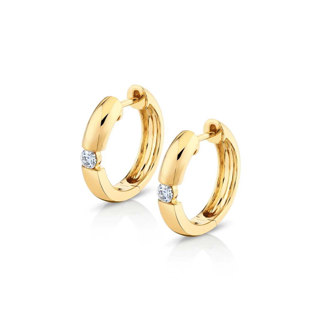 Two yellow-gold earrings are lying flat against a white background. The rounded hoop earrings feature a floating diamond in the center.