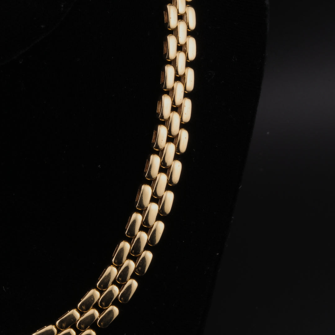 A close-up of the right side of the yellow-gold necklace featuring a three-row link design against a black background.