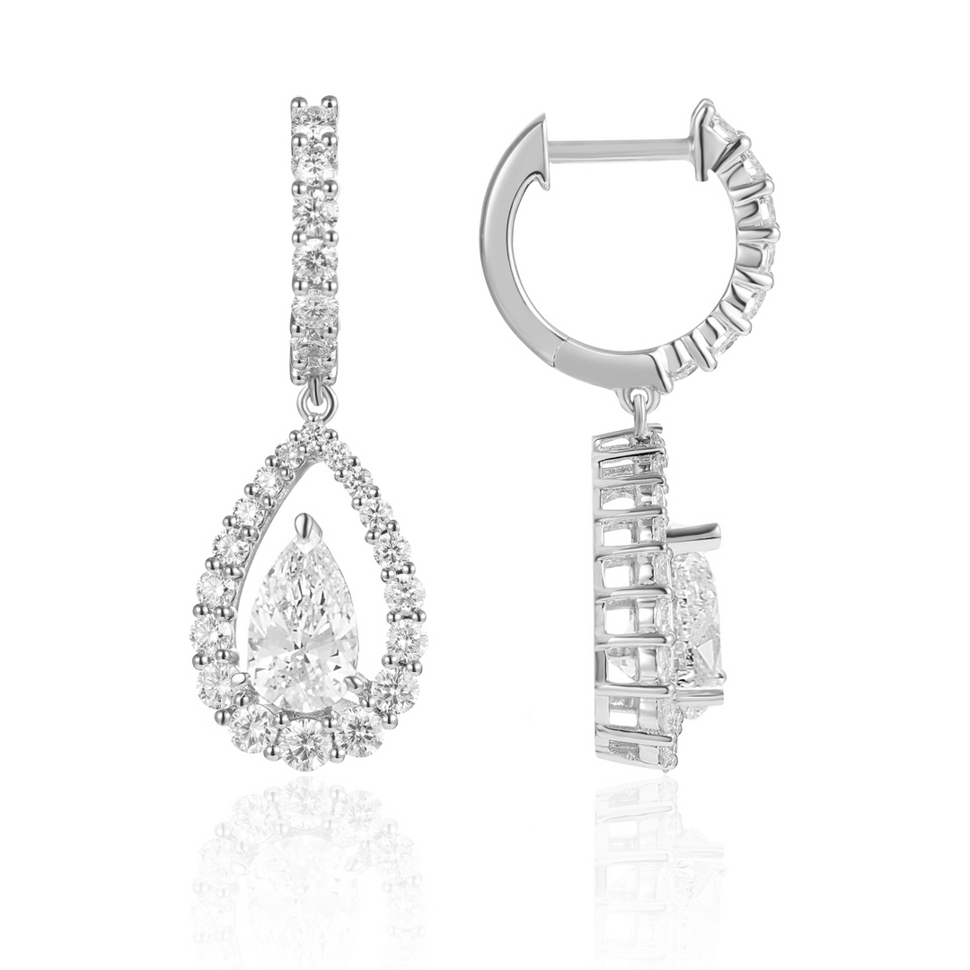 A pair of diamond dangle earrings with a teardrop shaped diamond in the center with a diamond set halo. The right earring is angled to the side.