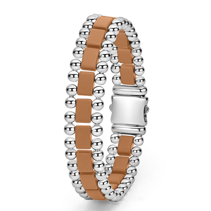 A stainless steel bracelet standing vertically in the middle of a white background featuring matte tan ceramic and caviar beading.