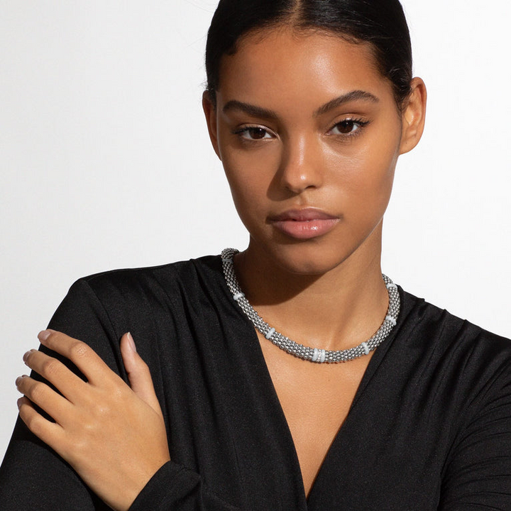 A woman is wearing a sterling silver and 18k gold necklace featuring white stations, one diamond set station, and caviar beading.
