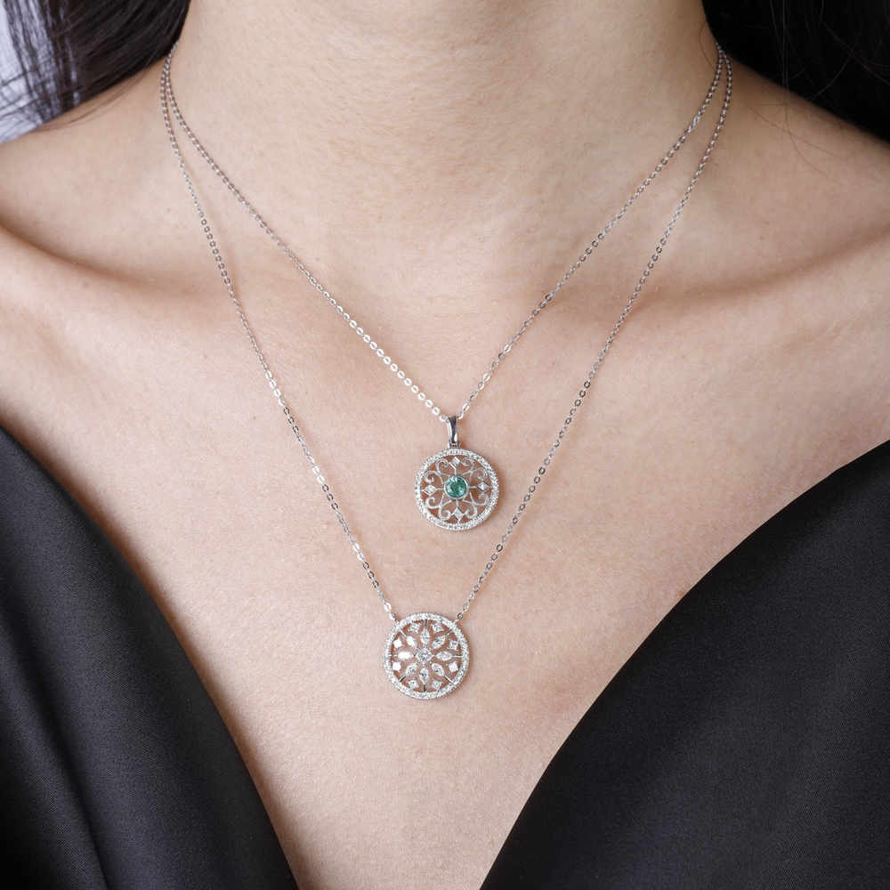 A woman is wearing a white-gold Filigree Necklace and a black blouse. The necklace features an emerald round diamond in the center with a twist design on the diamond-set pendant.