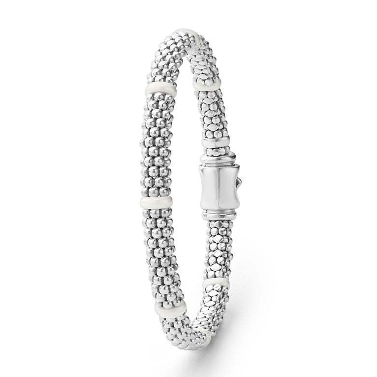 A sterling silver and ceramic beaded bracelet standing vertically in the middle of a white background featuring seven smooth white ceramic stations and silver Caviar beading.