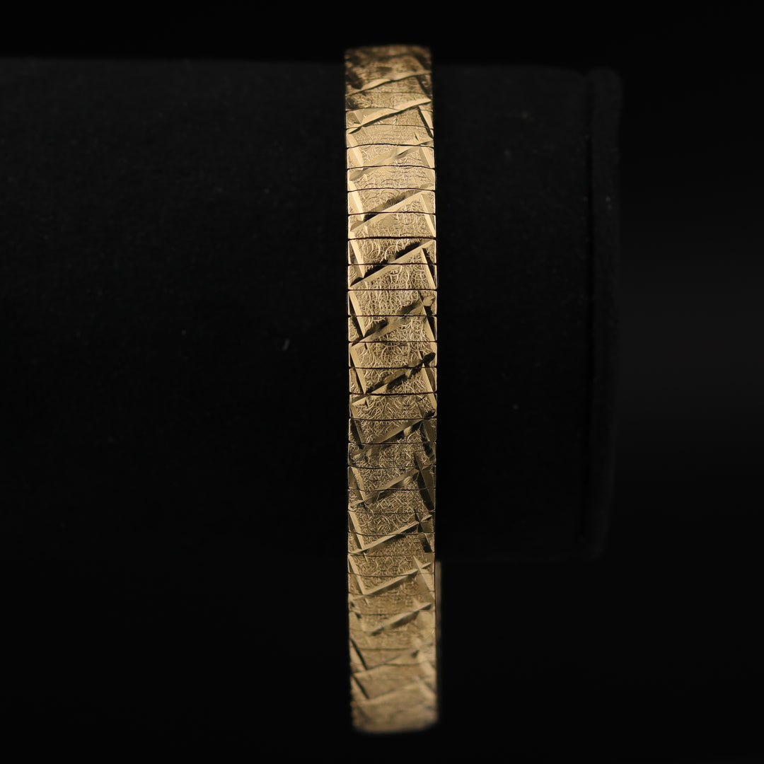 A close-up of a yellow-gold bracelet featuring intricate etching on the gold surface against a black background.