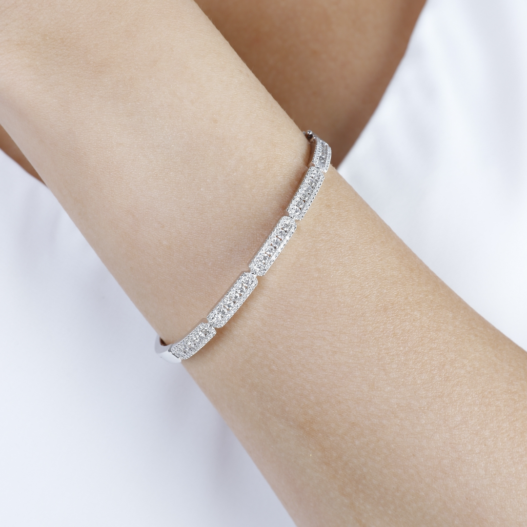 A woman is wearing a white top and bracelet made of 14k white gold with a pave diamond cluster design.