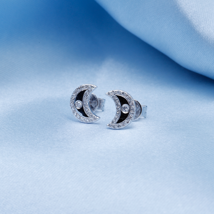 A pair of stud earrings with a half-moon design with sparkling diamonds that are set on the back against a light blue background.