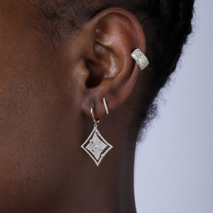 A woman with short black hair is wearing a pair of drop earrings with a mother-of-pearl Northstar motif and diamond-set halos. 