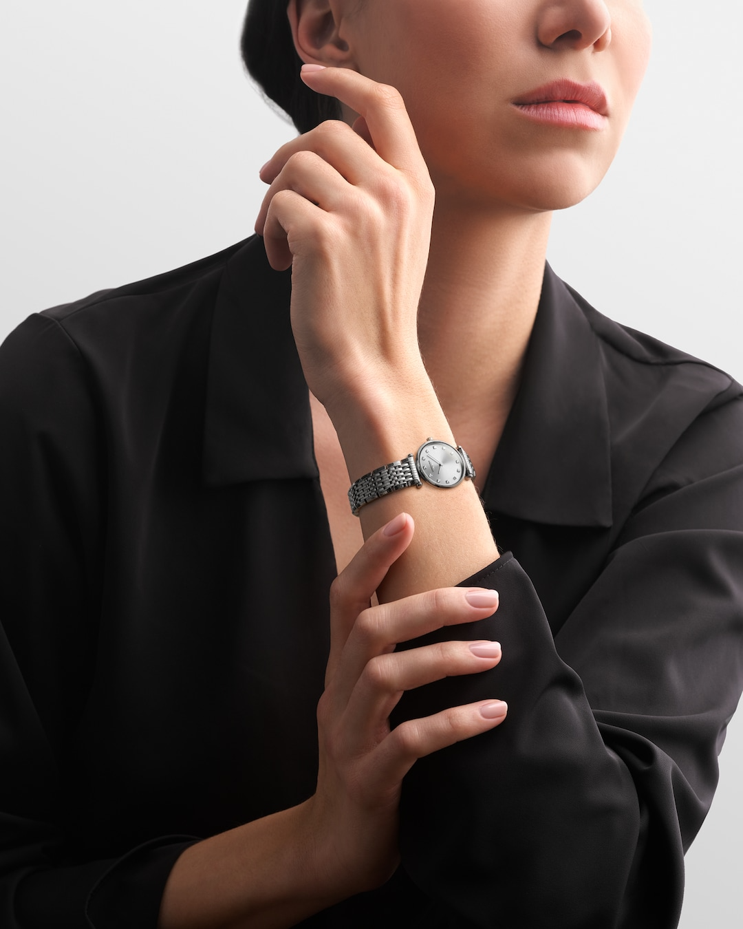 A woman wearing a black blouse and a Longines watch around her wrist. The watch features a silver diamond-set dial, silver hands and markers, a stainless steel bezel, and a stainless steel bracelet.