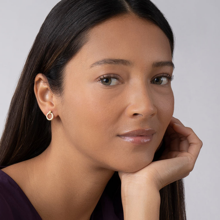 A woman wearing a black shirt and diamond gold circle stud earrings with an 18k gold Caviar accent