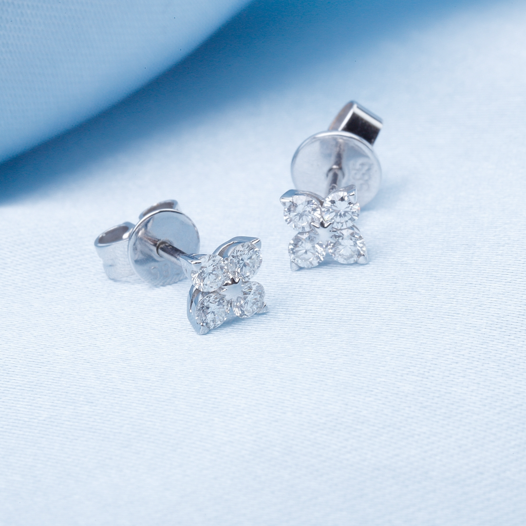 A pair of stud earrings with a flower design and round diamond clusters resting against a light-blue background.