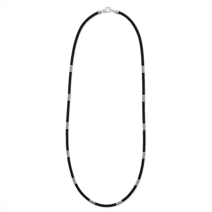 A sterling silver and ceramic beaded necklace in the middle of a white background featuring matte black ceramic and silver Caviar beading.