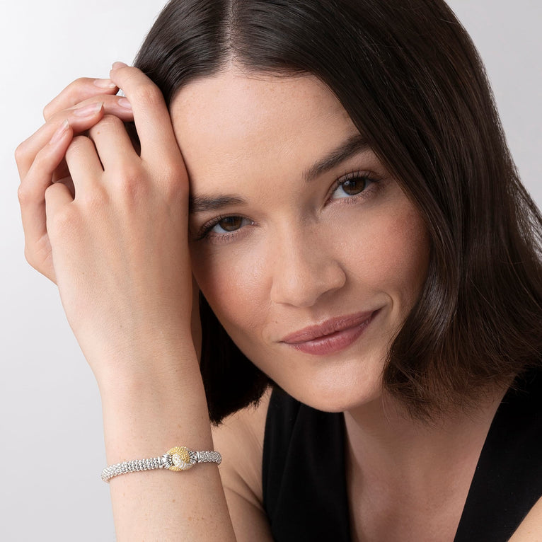 A close-up of a woman wearing a black top and a Sterling Silver & 18k gold bracelet. The bracelet features diamonds and gold women in a knot motif.