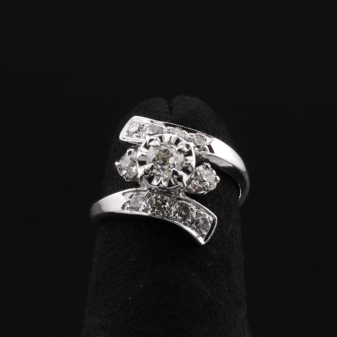 This is a close-up of a white-gold ring with a split shank. The band splits and elegantly hugs the top and bottom of the old mine-cut diamond. The ring rests on a black ring holder against a black background.