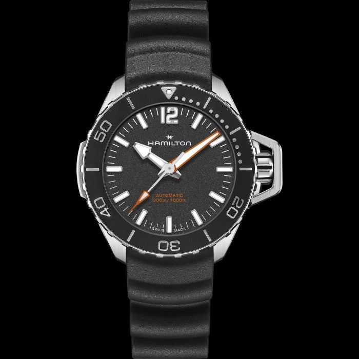 A Hamilton watch is laid out against a black background. It features a black dial, white hands and markers, a steel case, a black bezel, a steel crown, and a black rubber strap.