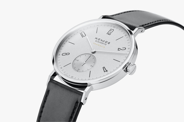 A side view of a Nomos Glashutte watch angled & curved to the left. It features a white dial, black and white hands and markers, a stainless steel bezel, and a black leather strap.