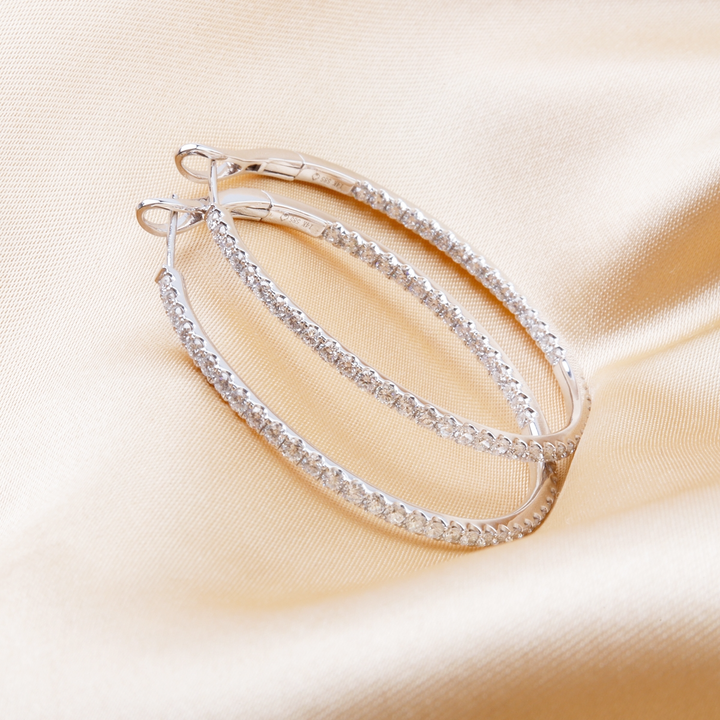 A pair of hoop earrings with a single row of round diamonds resting against gold background.