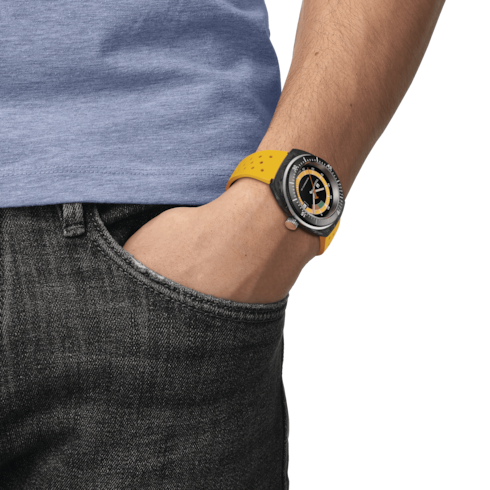 A man wearing a Tissot watch around his wrist. The watch features a black digital dial and a yellow rubber strap.