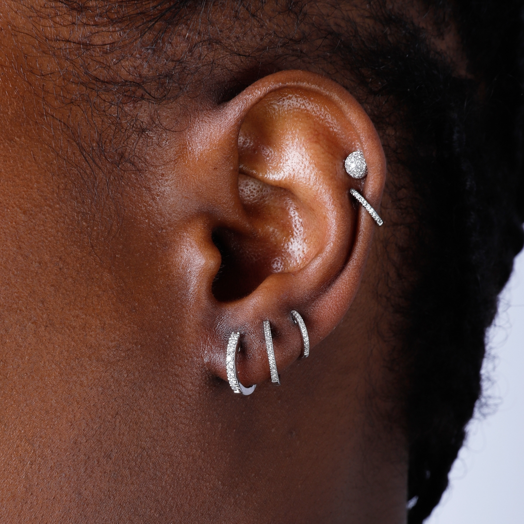 A woman with short black hair is wearing a pair of U-shaped huggies with a single row of round diamonds. 