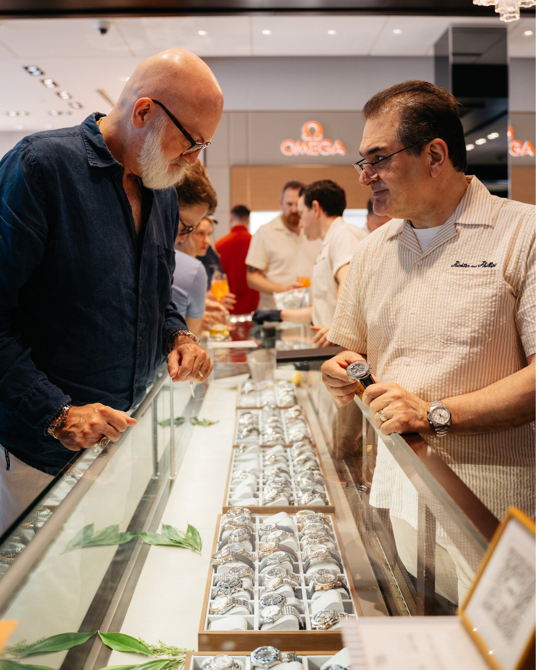 Two men examining jewelry in a store display case.
