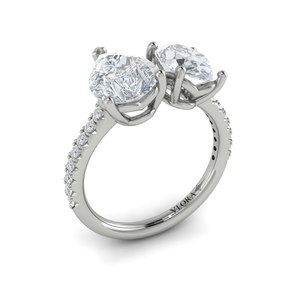 Angled view of an oval and pear toi et moi engagement ring showing the two raised settings and pavé diamond band.