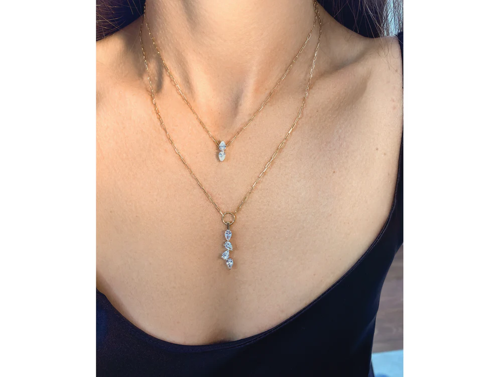 close up of a woman's neckline wearing two yellow gold diamond necklaces stacked together.