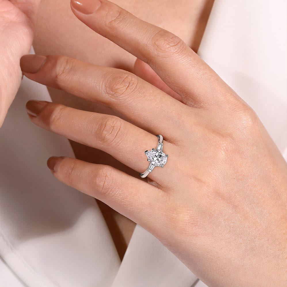 White gold pear three stone engagement ring worn on a hand, showing the pear-shaped center and baguette side diamonds.