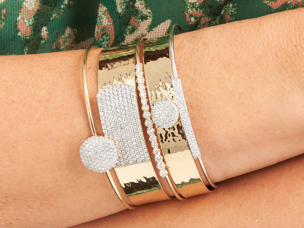 Close up of a woman's wrist wearing five different Yellow Gold and Diamond bracelets.