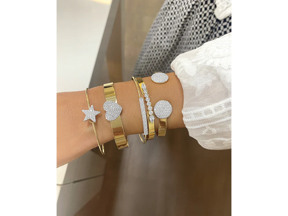 Close up of a woman's wrist wearing five different Yellow Gold and Diamond bracelets.