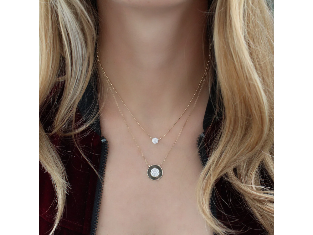 Blonde female wearing two stacked yellow gold diamond pavé necklaces with a black zippered jacket.