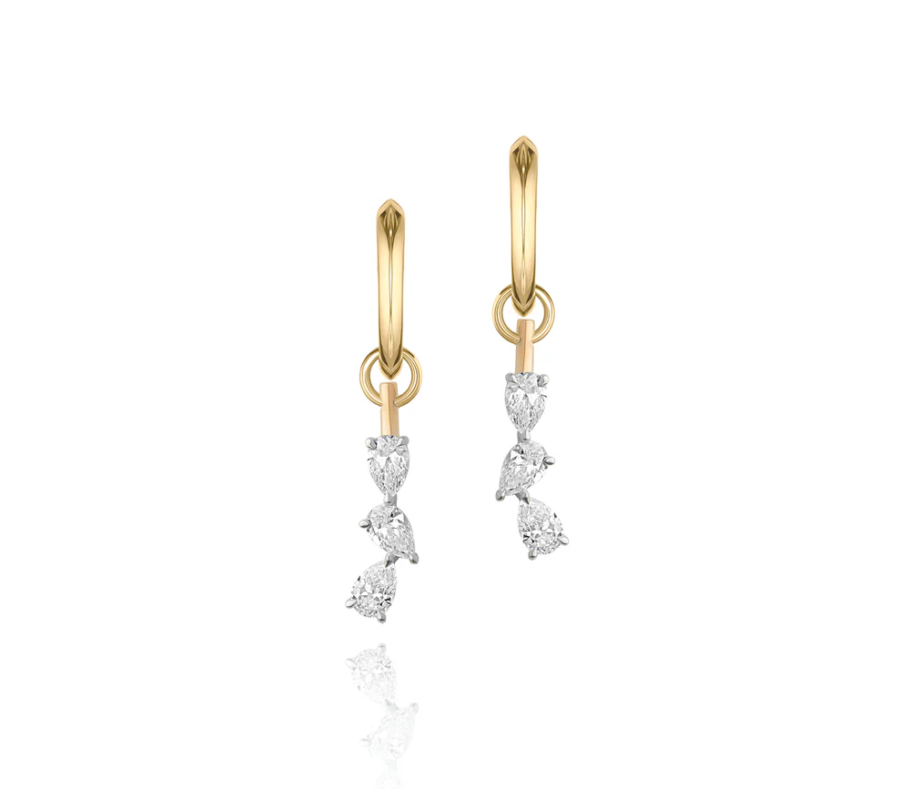 Close up of two yellow gold huggies with three pear shaped diamonds dangling from each one on a white background.