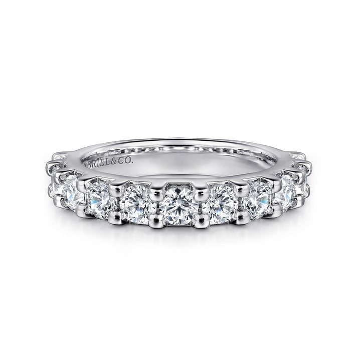 A white gold ring lies flat against a white background. The band features eleven round diamonds with a shared prong. 