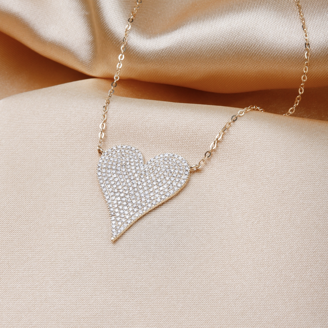 A close-up of a yellow-gold Pave Heart Necklace against a gold background. The necklace features a heart-shaped pendant with round diamonds.