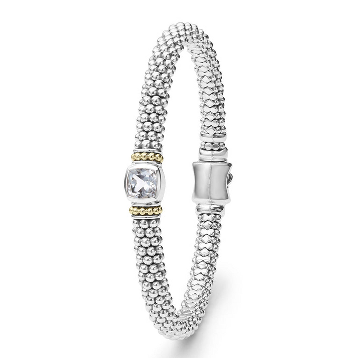 A sterling silver bracelet in the middle vertically of a white background features a white topaz gemstone and sterling silver Caviar beading with 18K gold detailing.