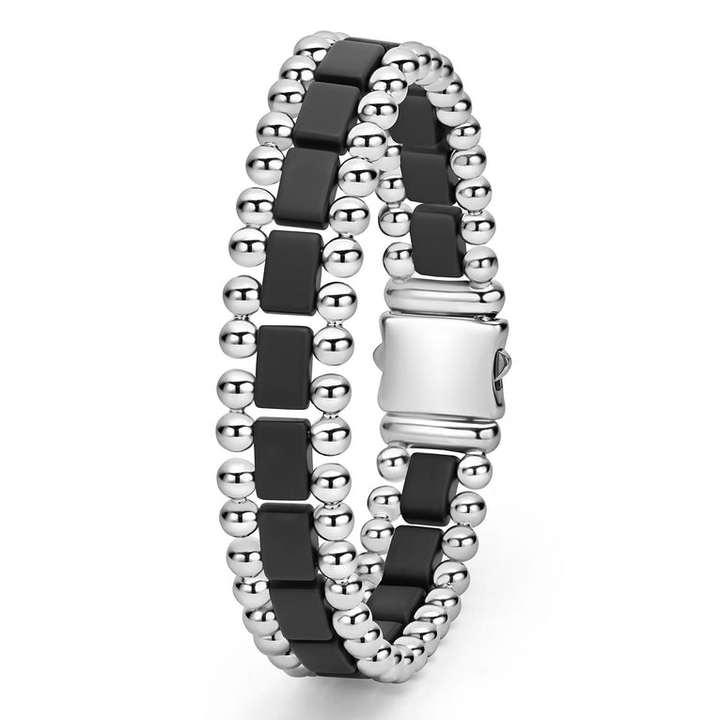 A stainless steel bracelet standing vertically in the middle of a white background featuring matte black ceramic and caviar beading.