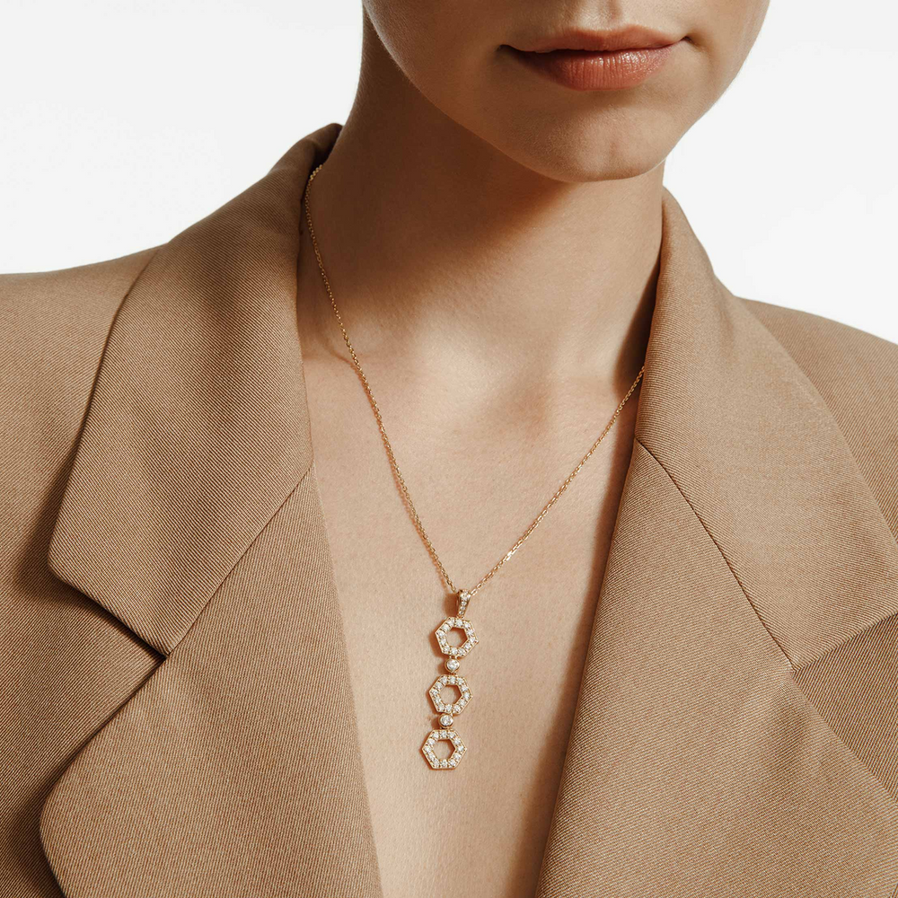 A close-up of a woman wearing a yellow-gold necklace. The necklace features three hexagon motif pendants with round bezel-set diamonds.