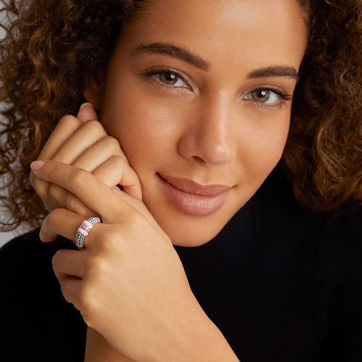 A woman is wearing a sterling silver ring featuring pink ceramic caviar beading with a row of diamonds.