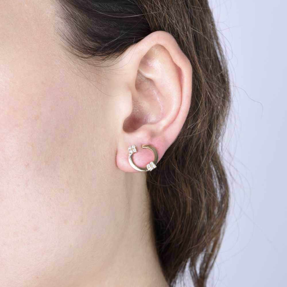 A woman with brunette hair is wearing a pair of stud earrings with an open circle with floral diamond motifs.