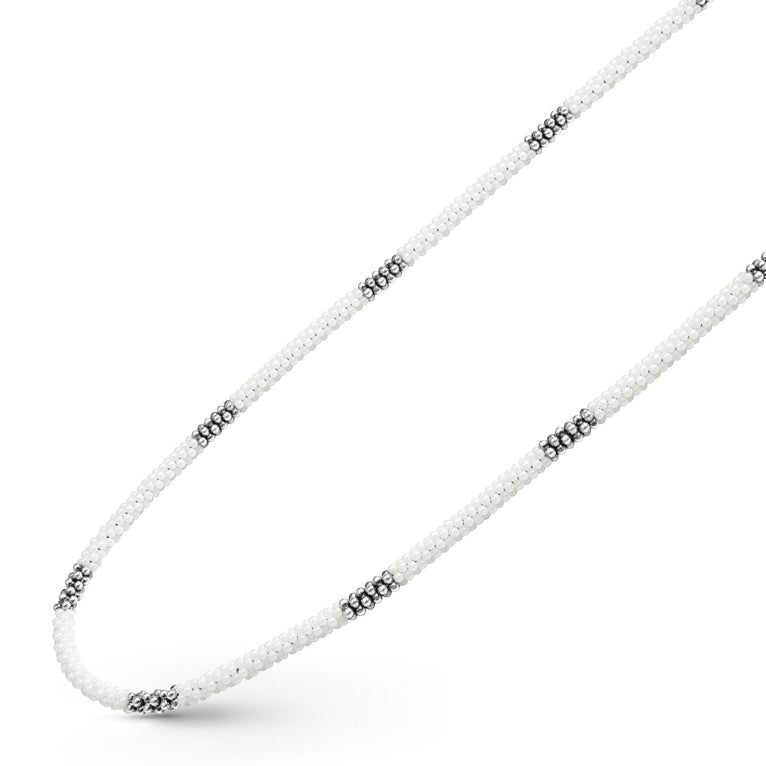 A sterling silver and ceramic beaded necklace angled to the right in the middle of a white background featuring white ceramic and silver Caviar beading.