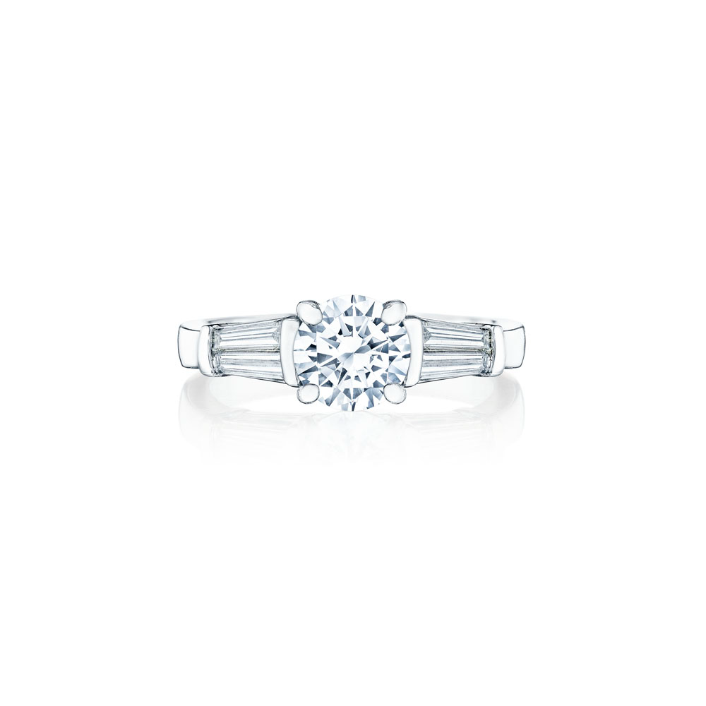 A white gold ring lies flat against a white background. It features a round-cut diamond set in the center with 4 tapered baguette diamonds.