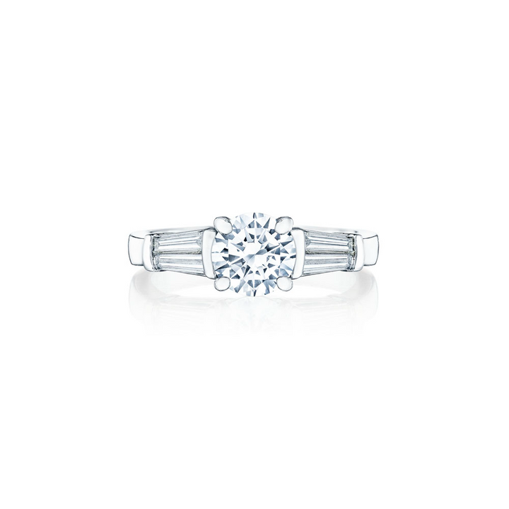 A white gold ring lies flat against a white background. It features a round-cut diamond set in the center with 4 tapered baguette diamonds.