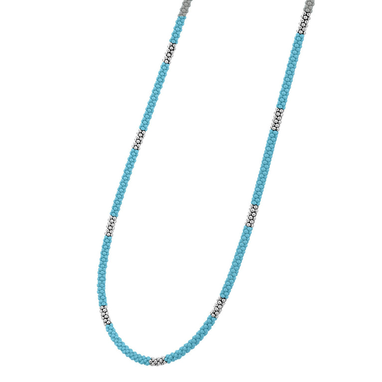 A sterling silver and ceramic beaded necklace angled to the right in the middle of a white background featuring light blue ceramic and silver Caviar beading.