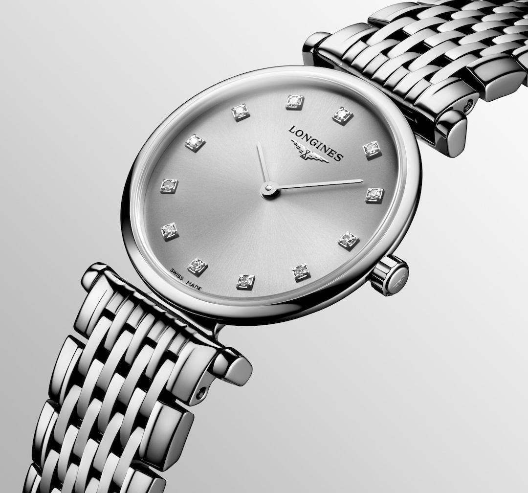 A Longines watch is displayed in the middle, angled to the right on a white background. The watch features a silver diamond-set dial, silver hands and markers, a stainless steel bezel, and a stainless steel bracelet.