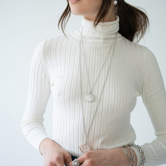 A woman wearing a silver locket necklace accented with a diamond in the center, beaded vertical stripes, and a floral pattern on the back.