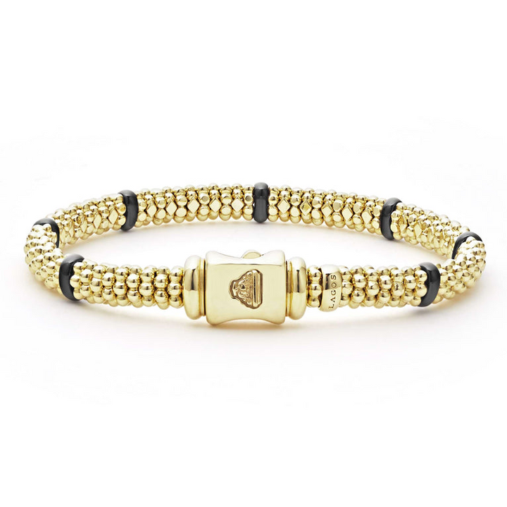 An 18k gold bracelet resting in the middle of a white background highlighting the gold clasp. The bracelet features smooth black stations and caviar beading.