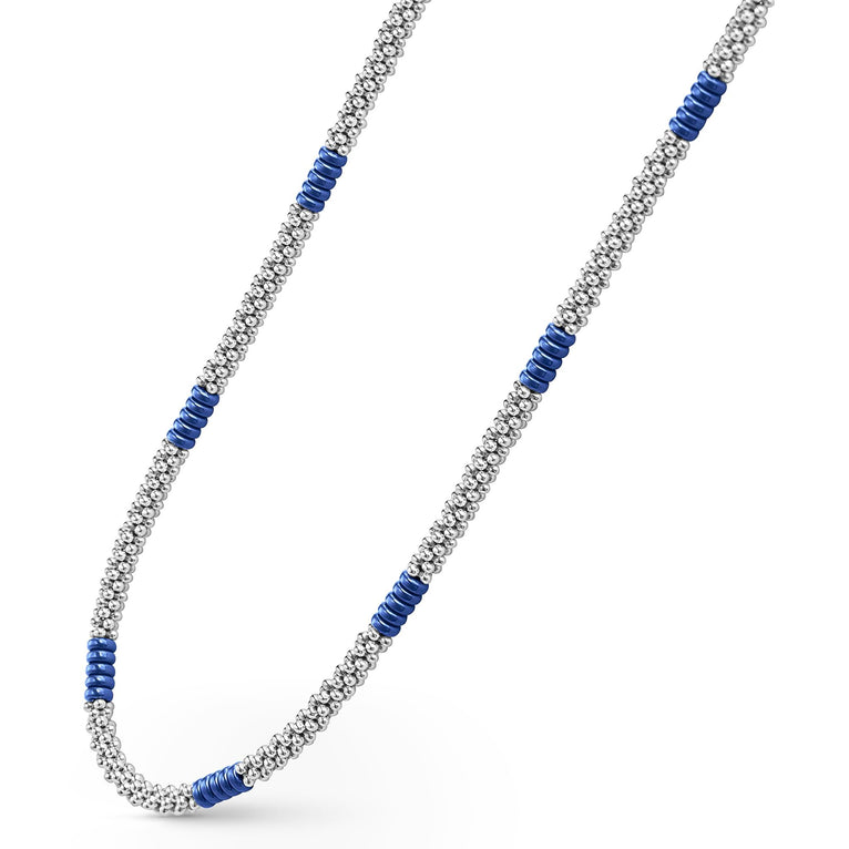 A sterling silver and ceramic beaded necklace angled to the right in the middle of a white background featuring blue ceramic and silver Caviar beading.