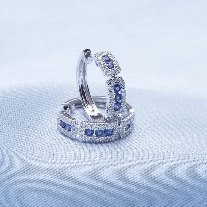 14k White Gold Hoop Earrings with stationed round diamonds. One earring is resting on the blue surface, and the other earring is standing, showing the side.