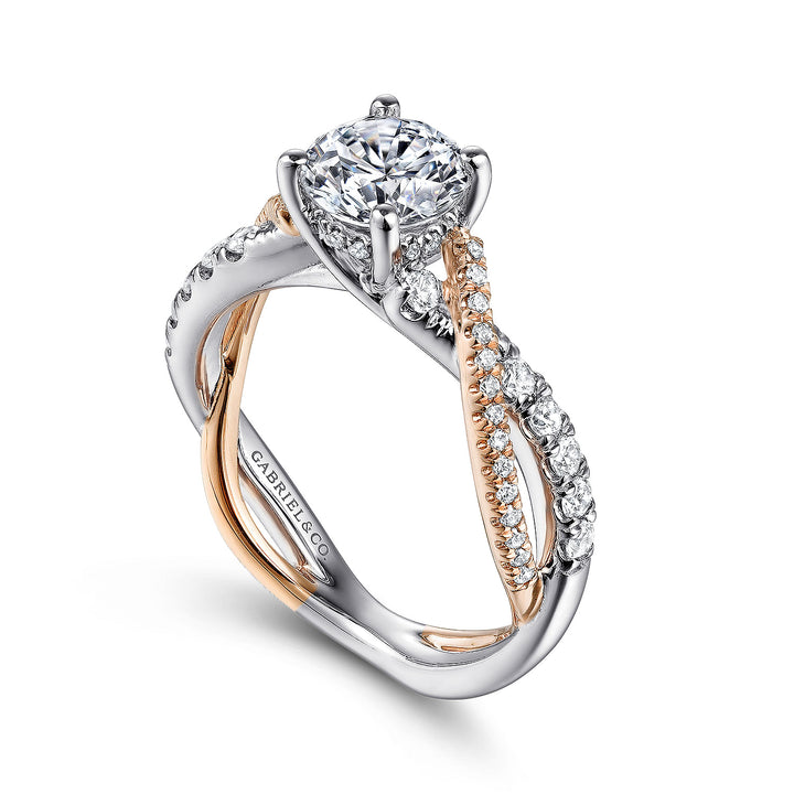 A close-up of a ring made of white and rose gold, angled to the left against a white background. It features a round-cut diamond set in the center with a twisted design band.